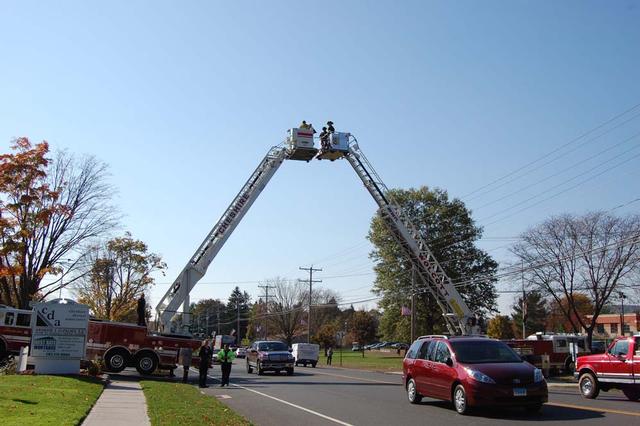 Cheshire and Wolcott ladder trucks position themselves to carry the stars and stripes over South Main Street in front of Cheshire High School.